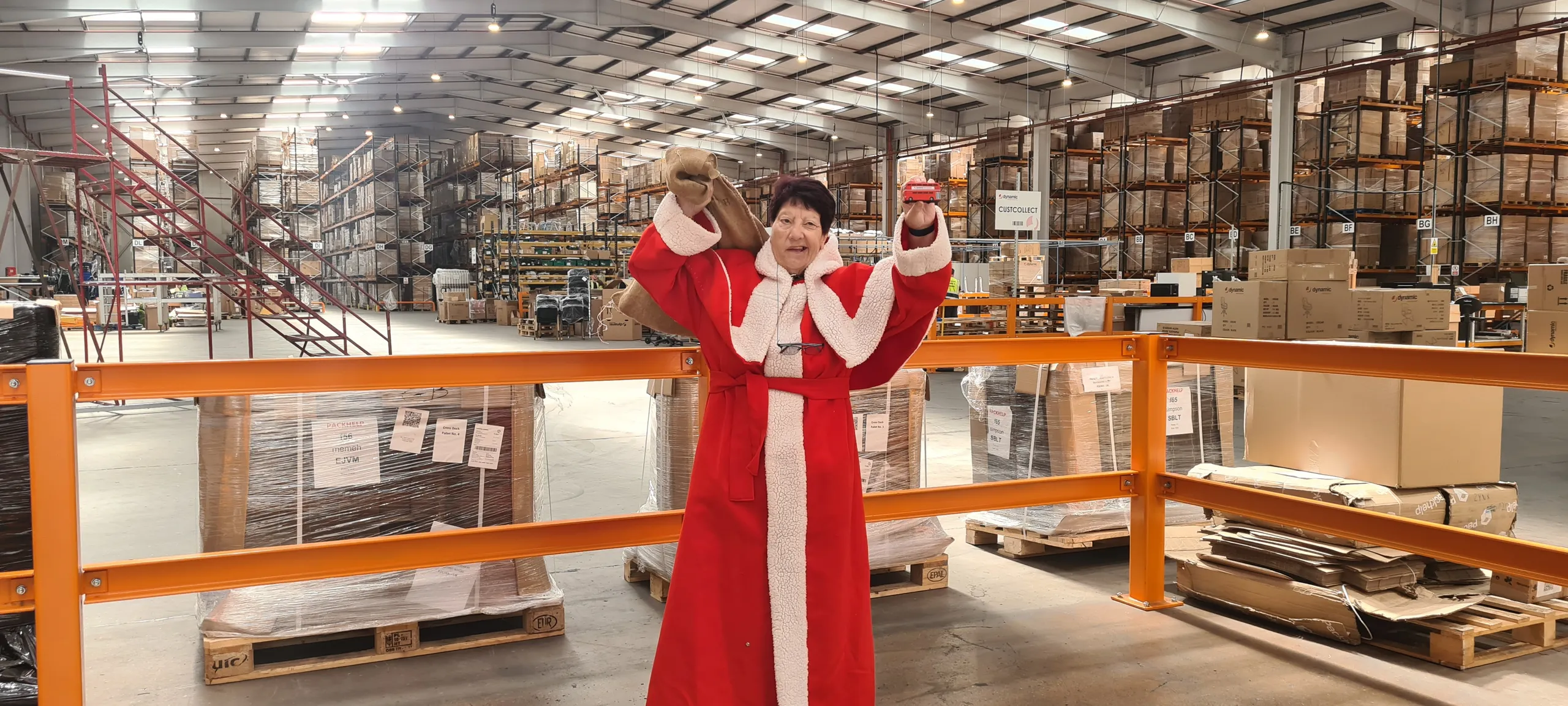 Jeanette Walsh in her Mother Christmas robe standing in a warehouse aisle lined with racking and pallets