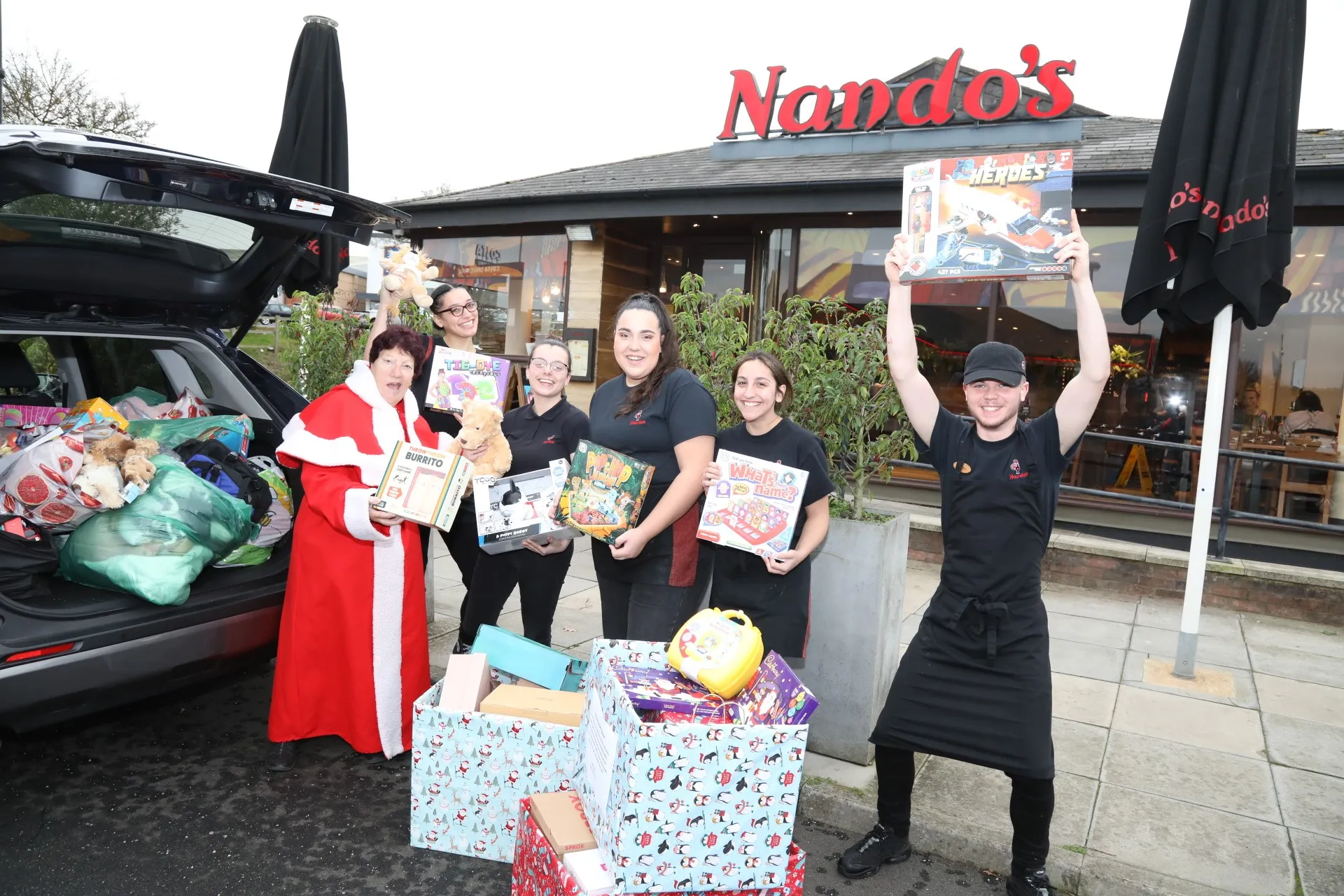 Jeanette Walsh and the Nando's team holding up donated toys and wrapped gifts outside the restaurant