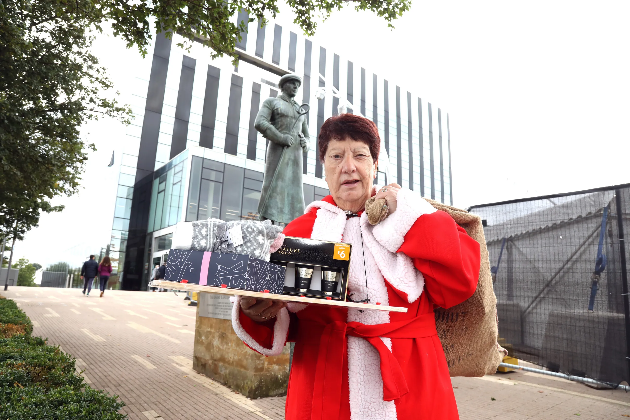 Jeanette Walsh in her Mother Christmas robe carrying a box of donated gifts outside a modern building
