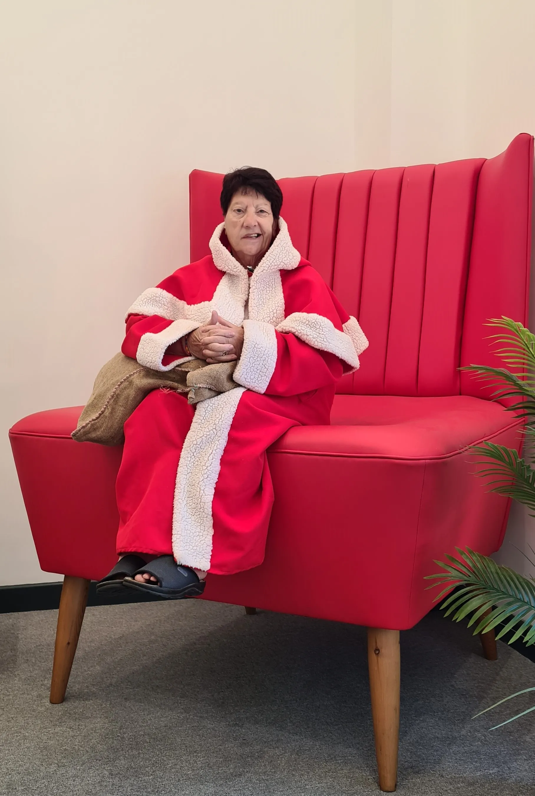 Jeanette Walsh sitting in a red armchair wearing her Mother Christmas robe