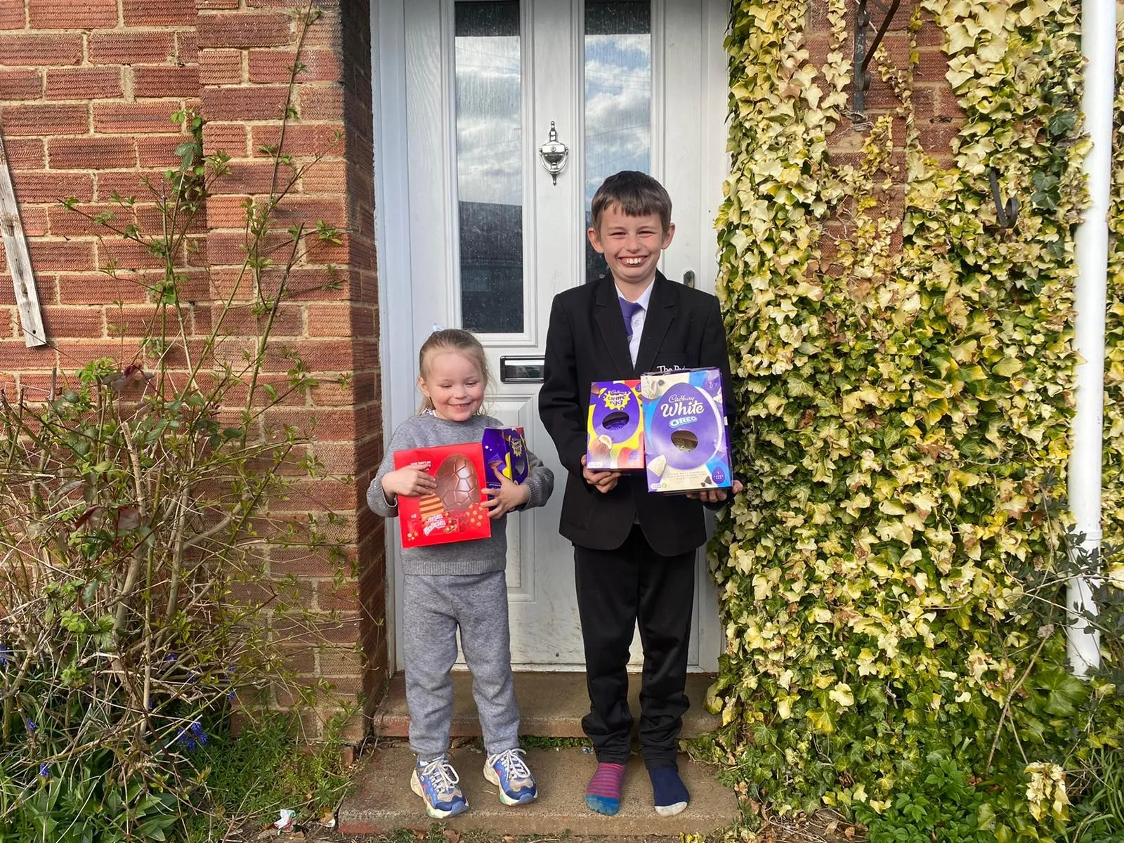 Two young boys at a front door holding the Easter eggs they have been given