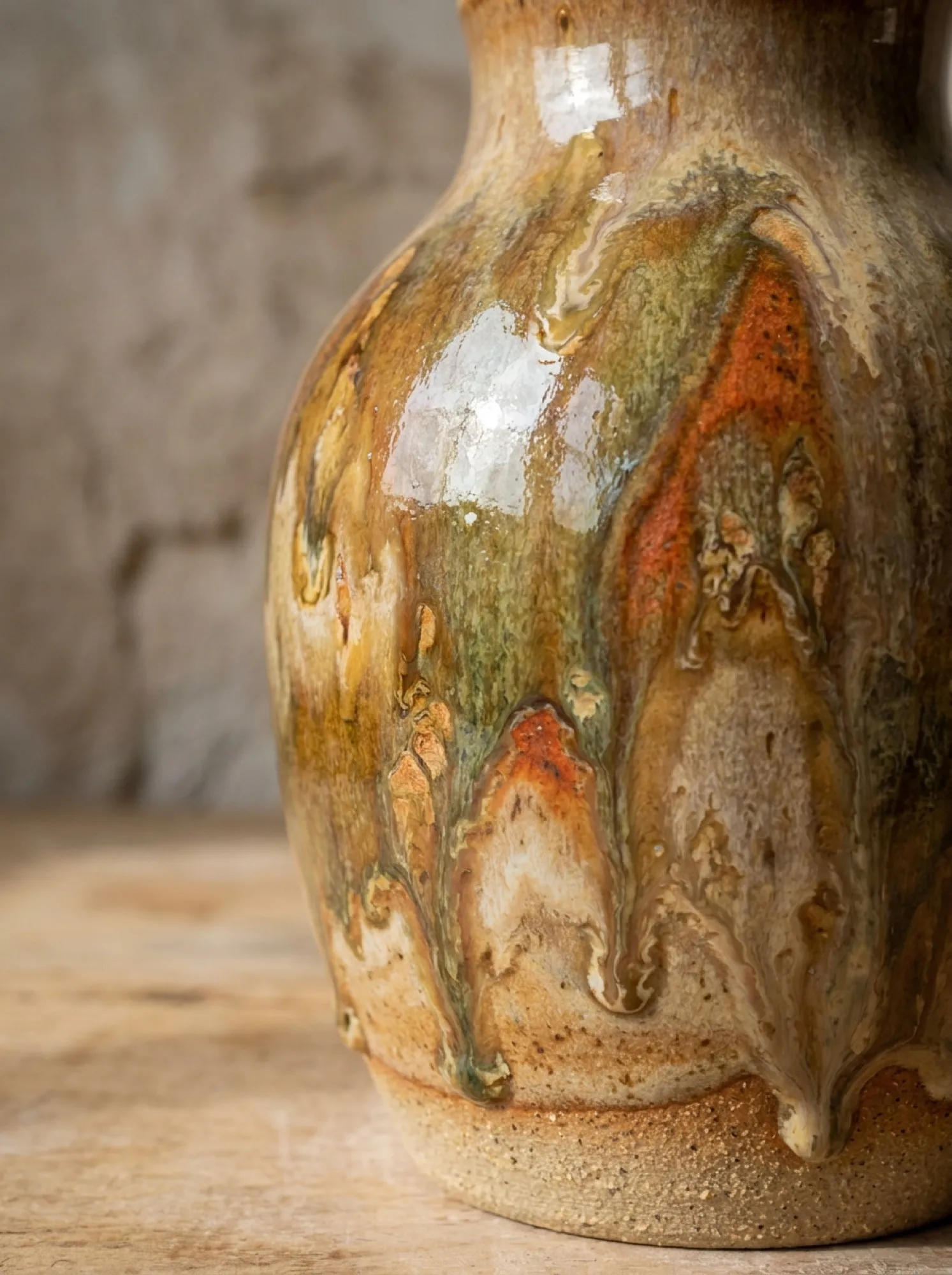 Close-up of a hand-glazed stoneware vase with amber and green drips
