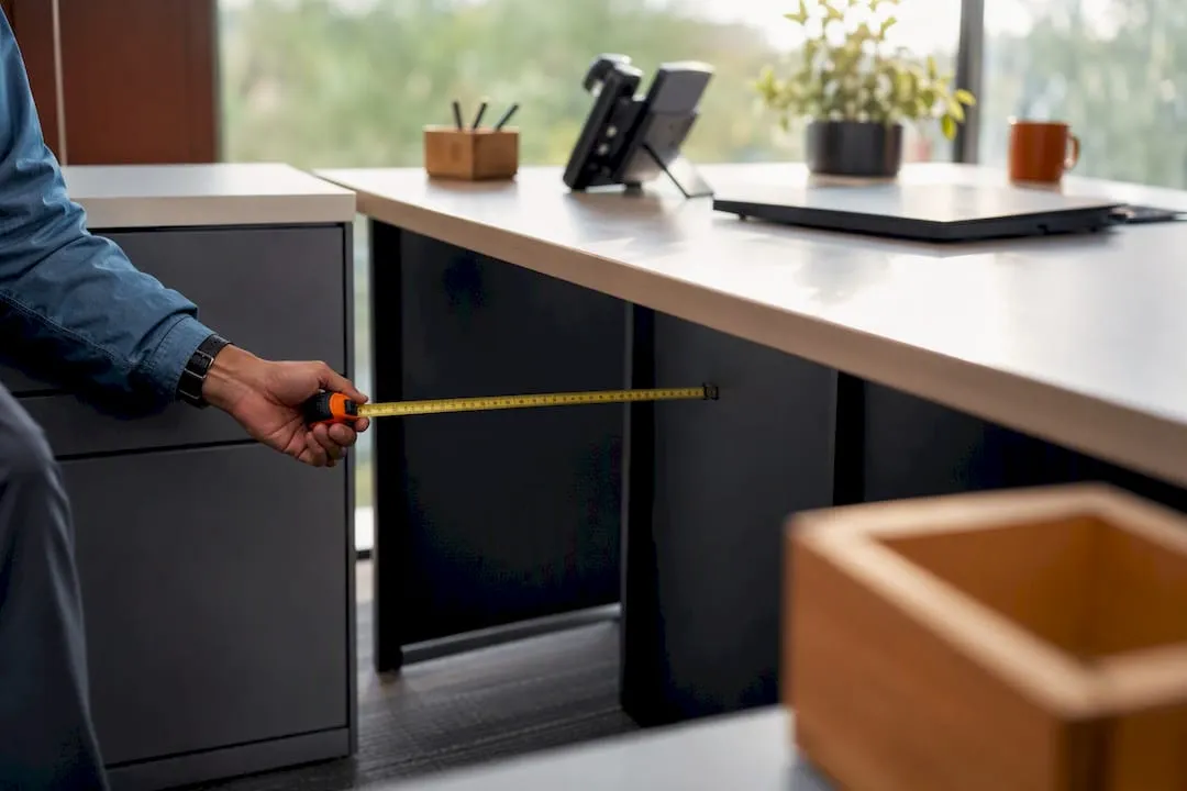 Hand measuring L-shaped desk corner clearance
