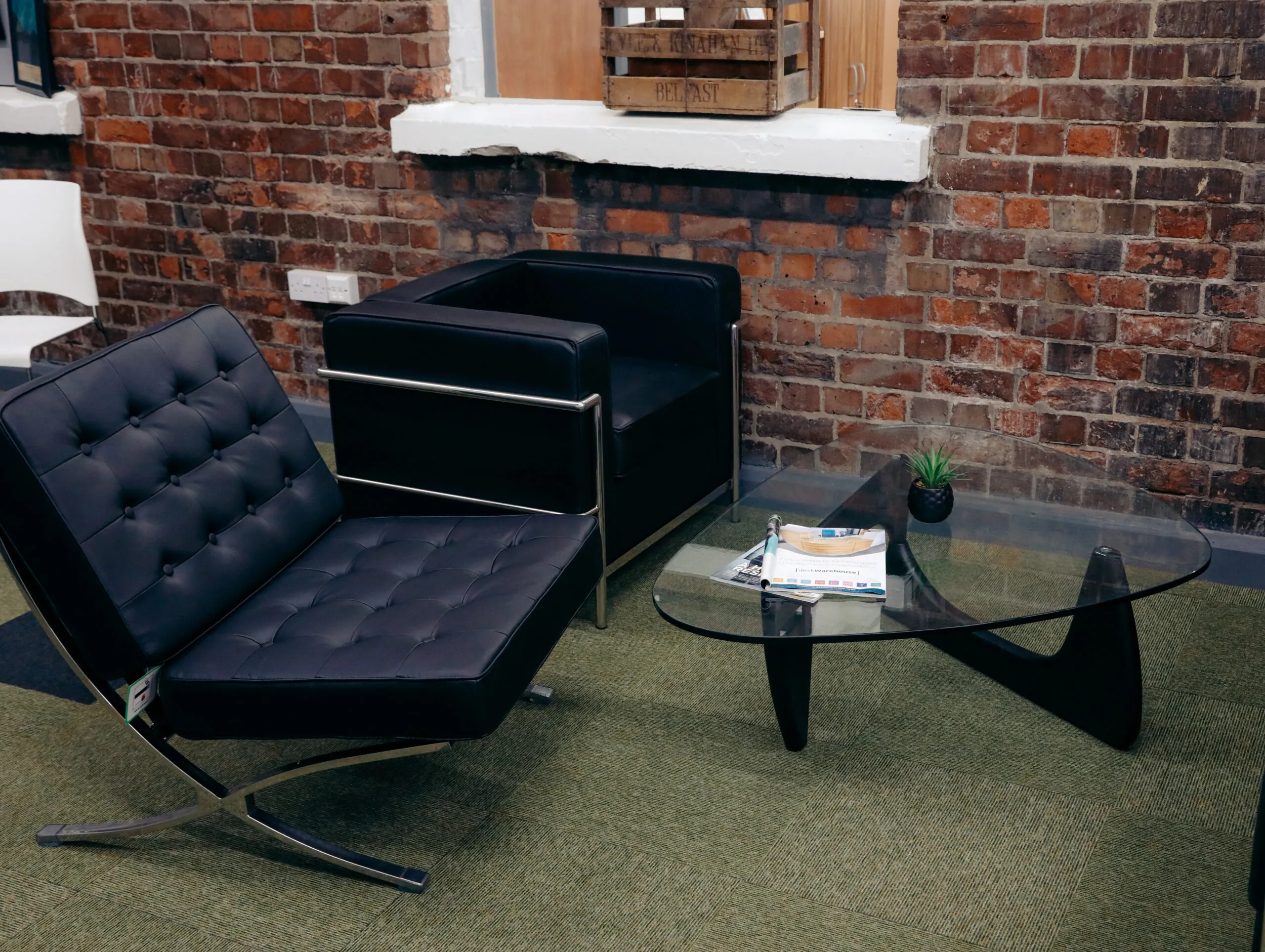Black leather lounge chair, sofa and glass coffee table against a brick wall