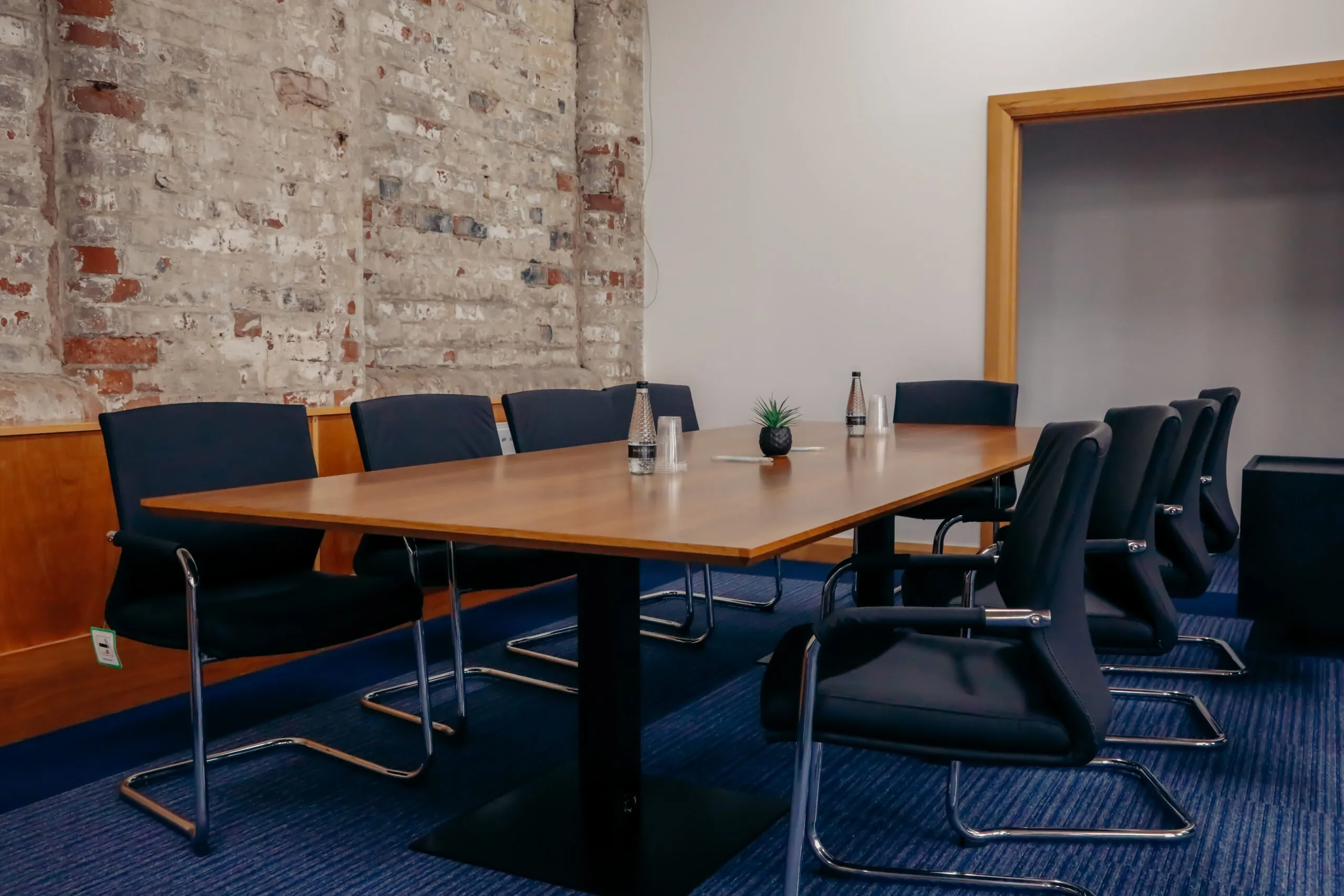 Walnut boardroom table with black chairs and exposed brick