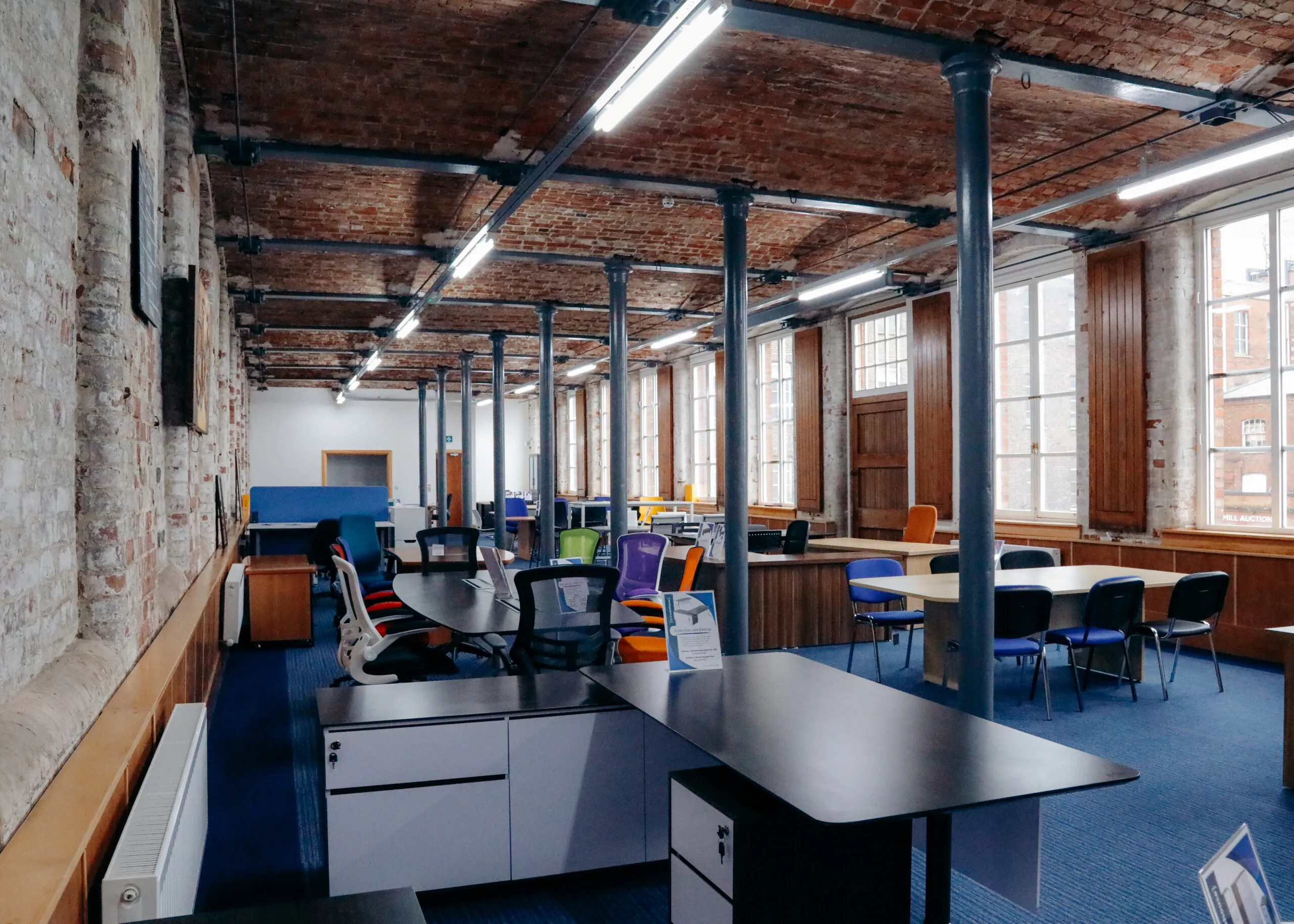 Showroom with black desks and colourful chairs under brick vaults