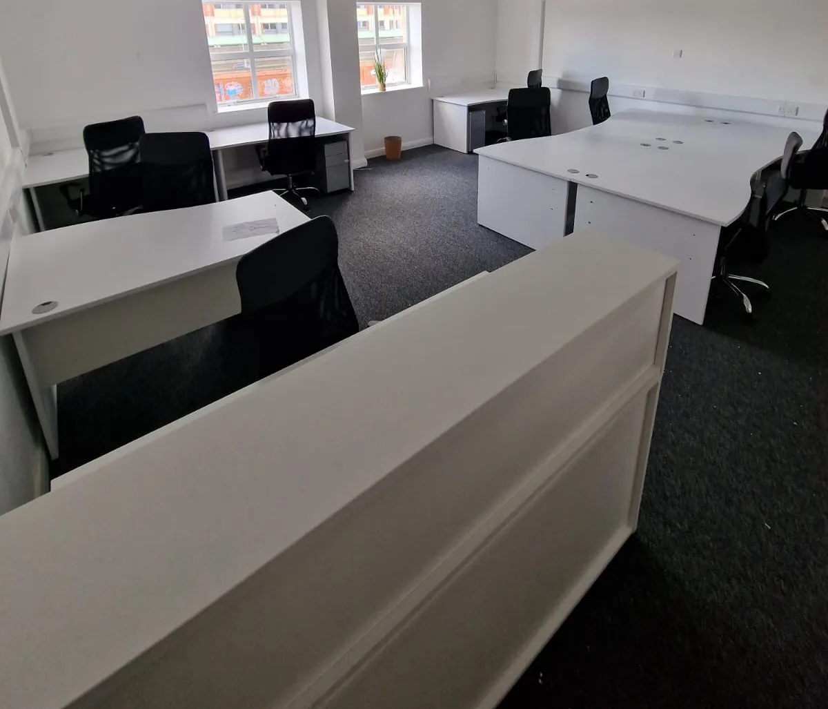 Open-plan office with white desks, black mesh chairs and a white storage wall