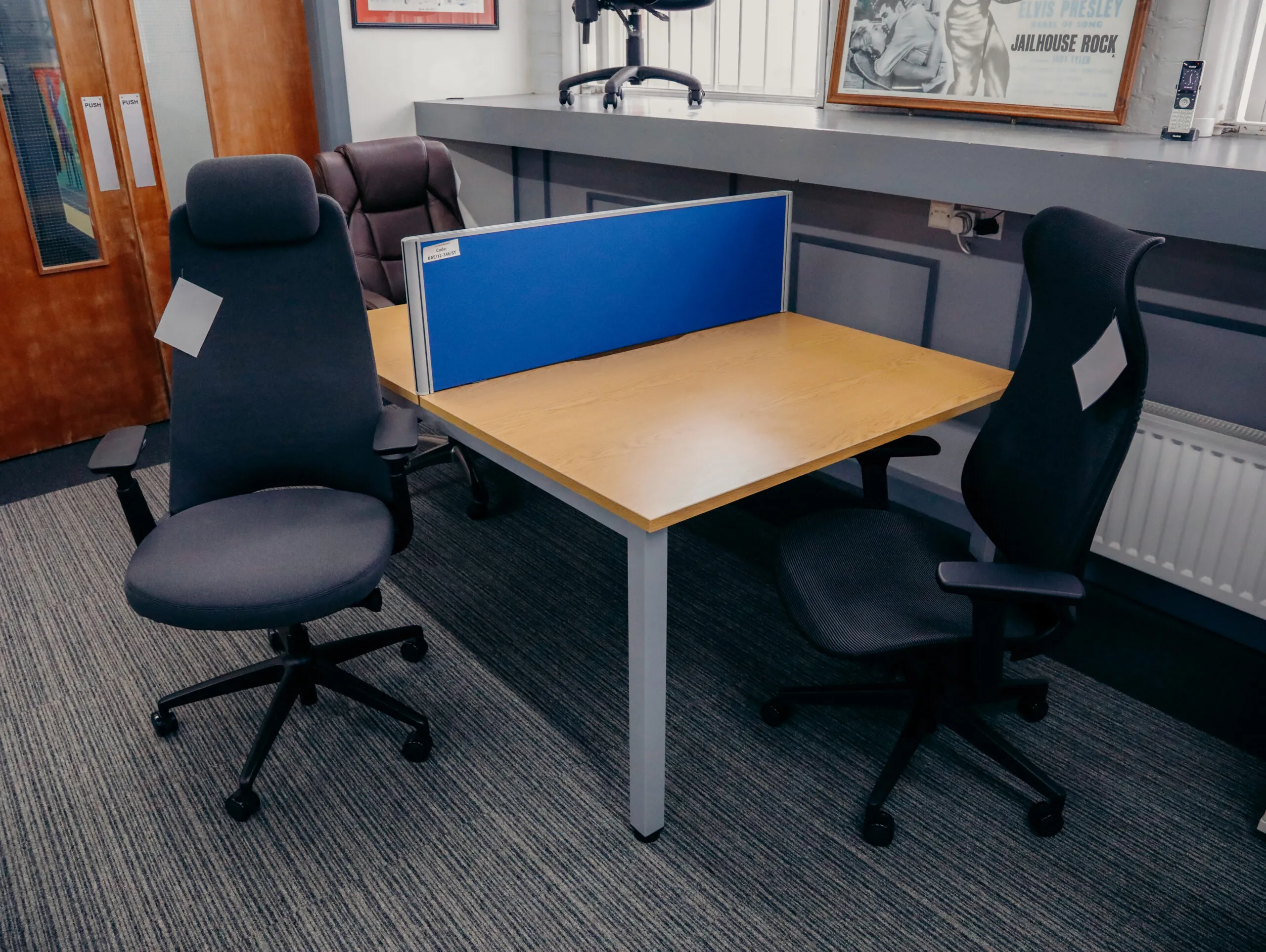 Oak desk with a blue screen and two black chairs