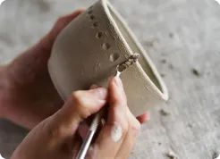 Hands texturing a clay cup with a tool