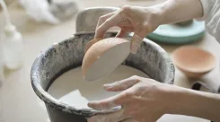 Hands dipping a bowl into a bucket of glaze